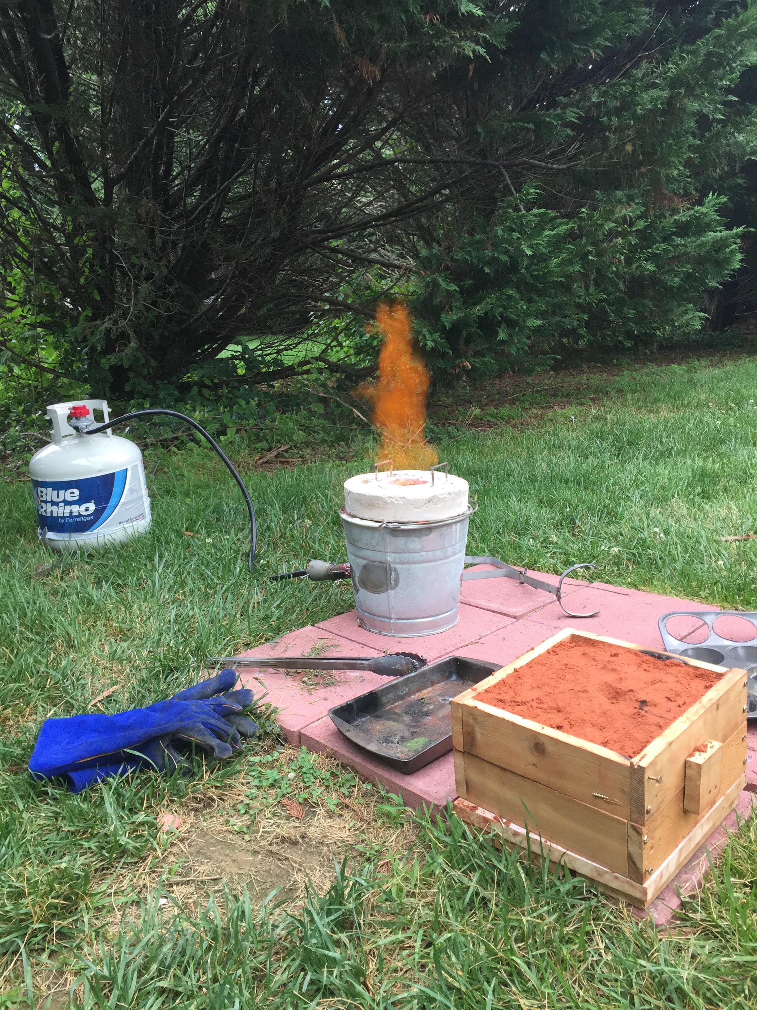 Metal foundry running outdoors — crucible at temperature with propane burner and casting mold